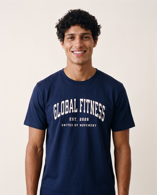 A smiling man with curly dark hair wearing a navy blue crewneck t-shirt with 'GLOBAL FITNESS EST. 2026 UNITED BY MOVEMENT' printed in white on the front, set against a plain light beige background.