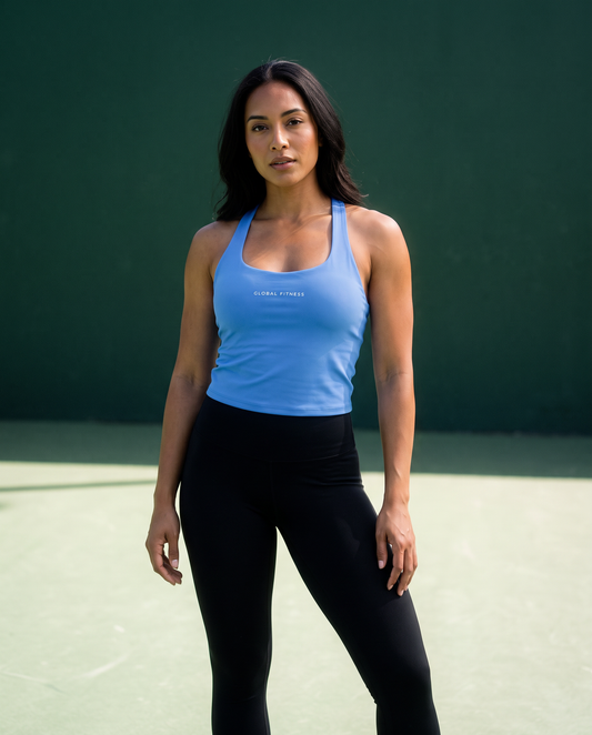 A woman stands on a tennis court wearing a light blue athletic tank top with 'ALPHA FITNESS' printed on the chest and black leggings.